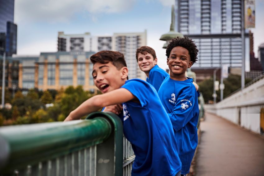 Three Scouts smiling and leaning on a bridge in an urban setting