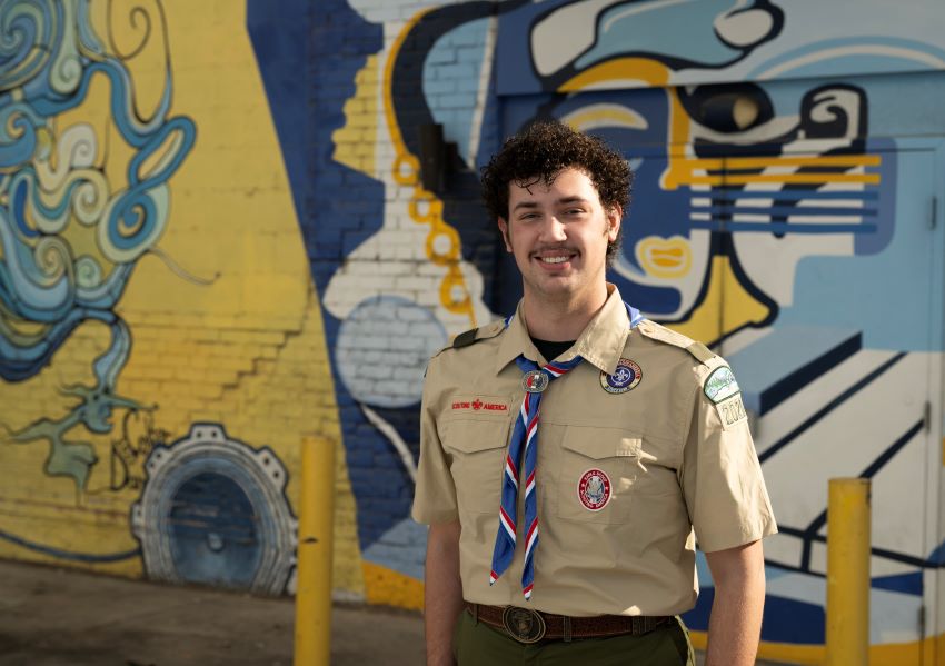 Young Eagle Scout in uniform standing in front of a colorful mural, representing Scouting achievement and leadership.