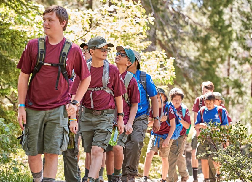 Group of Scouts hiking on a forest trail, wearing backpacks and enjoying a team-building adventure in nature.