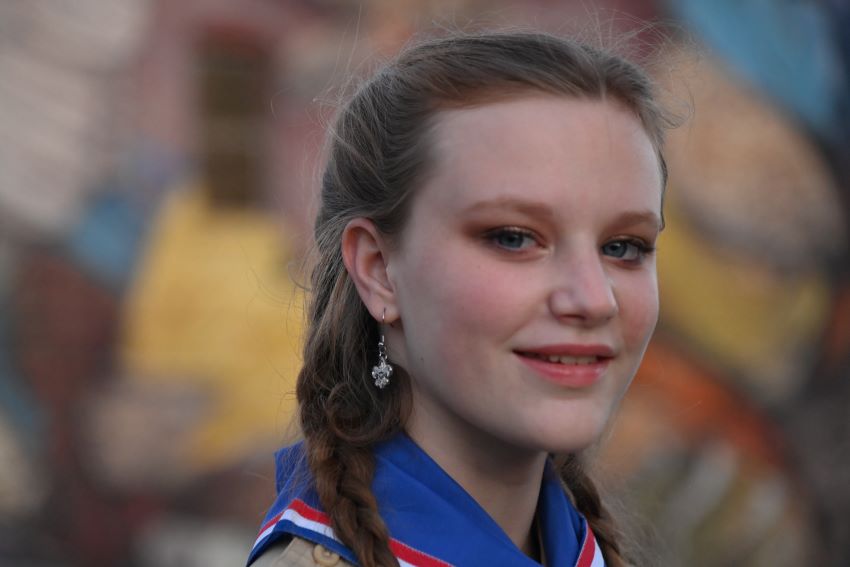 Close-up of a smiling Scout in uniform, showcasing leadership and pride against a colorful background.